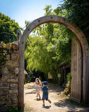Two children run through an archway at Abbotsbury Subtropical Gardens in a sunny, green setting.
