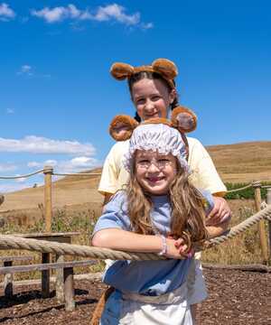 Two children wearing animal-themed hats pose together outdoors with a clear blue sky.