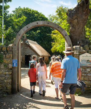 Visitors walking through the arched entrance to Abbotsbury Swannery surrounded by greenery.
